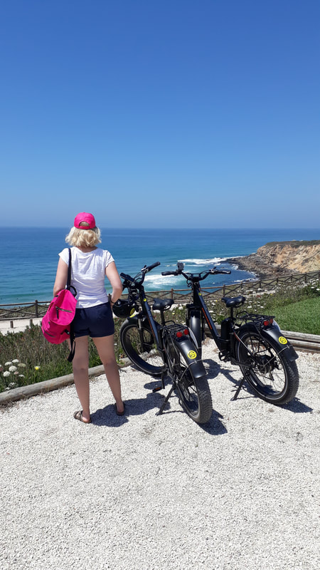 Attractive woman standing by two ebikes looking at the Atlantic ocean in Sintra