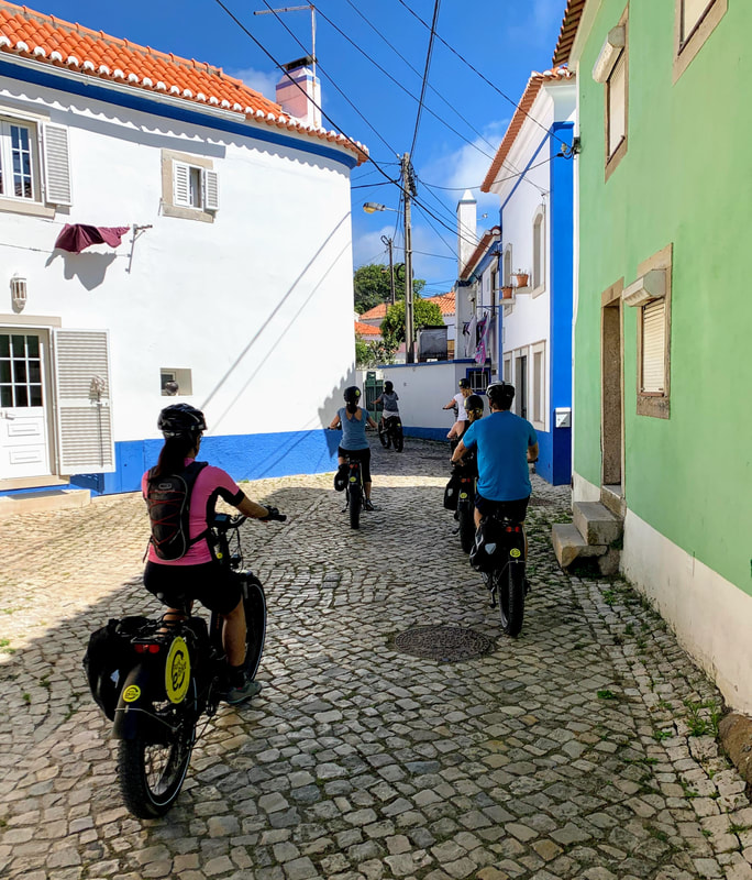 Family on ebikes cycle on a cobbled street through a village in Sintra 
