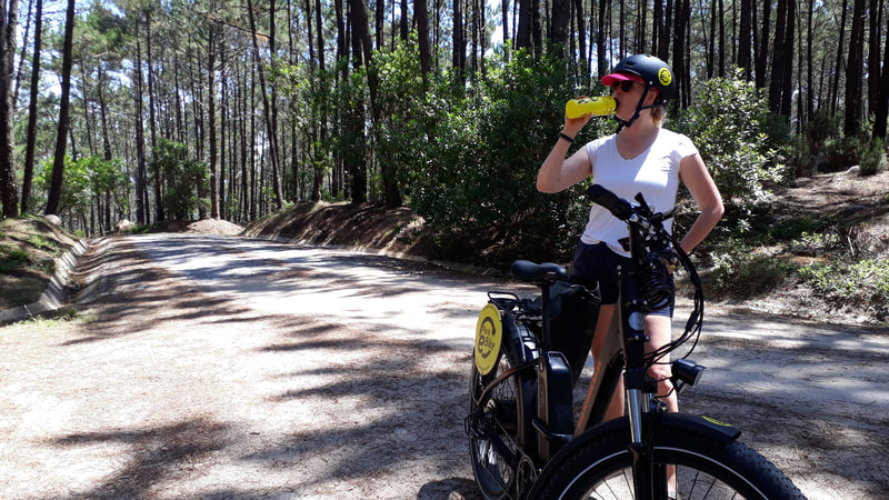Young woman on a forest trail drinking from a sports bottle beside her ebike